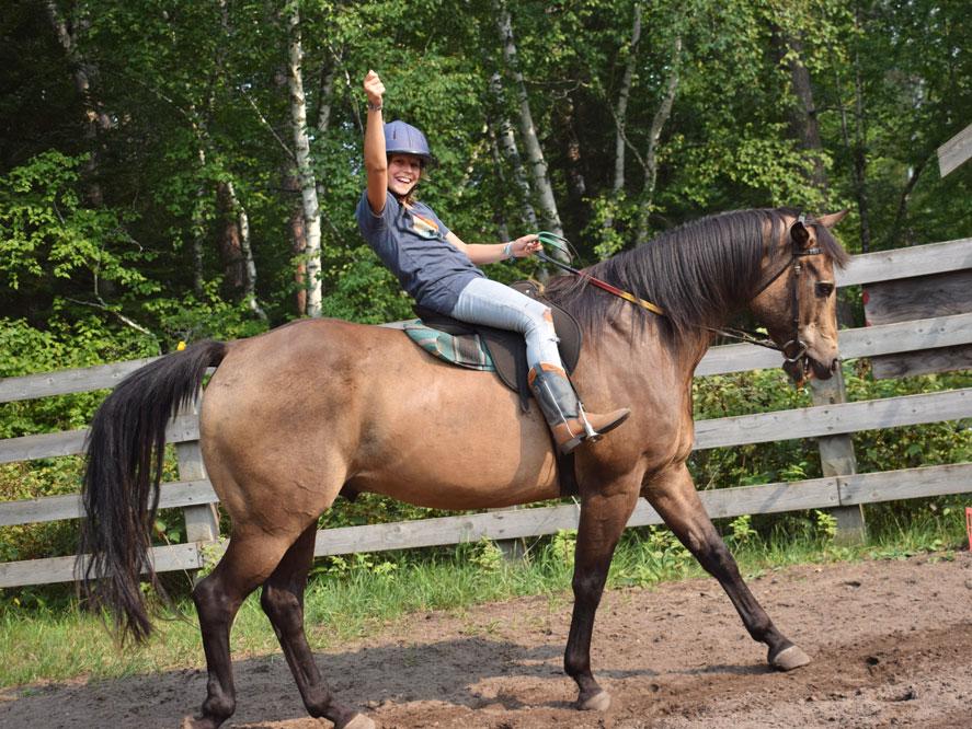 Young girl learning to trot on a horse at a riding camp