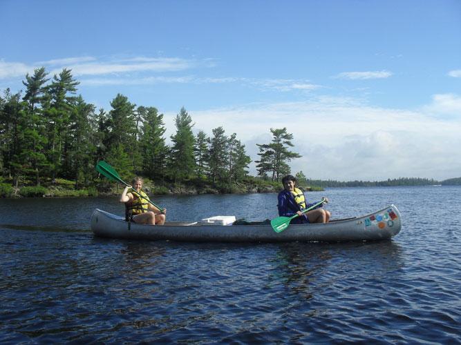 Campers paddling canoes on a lake at a wilderness sleepaway camp